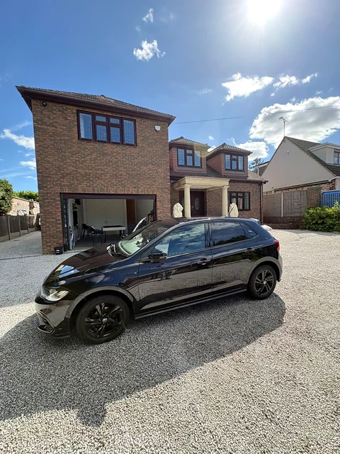 Black hatchback viewed from the side in front of a brick house