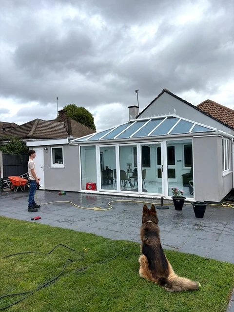 A conservatory, paved patio, cleaning hose, a person and a dog in the garden